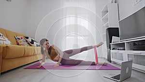 On-line work out woman using internet services with help of her instructor. Woman lays on mat and lifts leg with