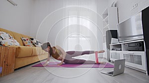 On-line work out woman using internet services with help of her instructor. Woman lays on mat and lifts leg with