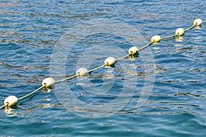 Line of yellow buoys against the blue sea. Restriction on open water. Glare and ripples on the water