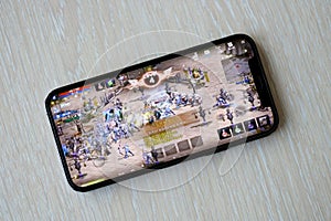 Lineage M mobile iOS game on iPhone 15 smartphone screen on wooden table during mobile gameplay