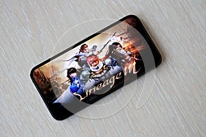 Lineage M mobile iOS game on iPhone 15 smartphone screen on wooden table during mobile gameplay