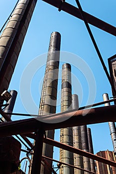 Lines of smokestacks, pipes, and girders silhouetted against a blue sky, old industrial complex