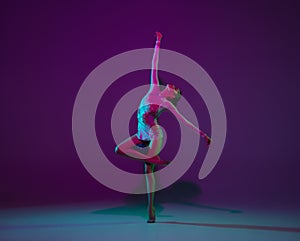Young female athlete, rhythmic gymnastics artist on purple background with neon light. Beautiful girl practicing with photo