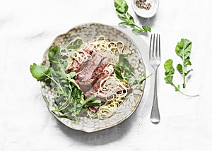 Linguine pasta with sliced beef steak and rocket salad on a light background, top view
