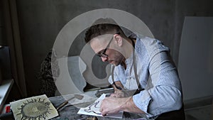 Linocut artist in apron at workplace using cutting instrument