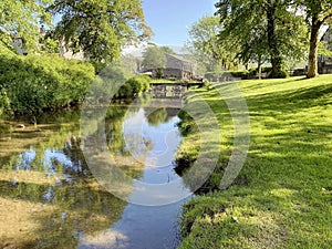 Linton Beck, with old trees, a stone bridge, and buildings in Linton, Yorkshire, UK