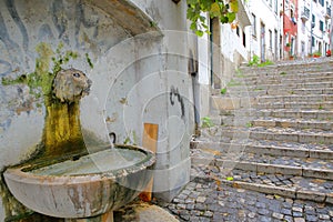 A lion`s head fountain in Alfama neighborhood with cobbled stairs in Lisbon, Portugal photo
