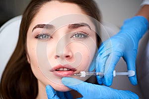 Lip Augmentation. Closeup Of Beautician Doctor Hands Doing Beauty Procedure To Female Lips with Syringe. Young Woman`s