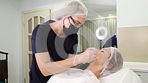 Lip augmentation procedure. Surgeon, in medical mask and gloves, kneads and massages female lips to evenly distribute