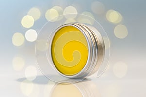 Lip balm in metal jar over light bokeh background