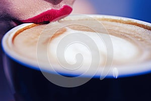 Lips girl touch the cup with coffee. Coffee mug with heart shape on the froth. Closeup of cappuccino surface with heart