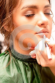 Lips makeup. Makeup artist applies contour with a pencil to the lips of a young woman in a beauty salon.