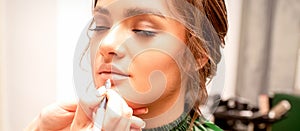 Lips makeup. Makeup artist applies contour with a pencil to the lips of a young woman in a beauty salon.