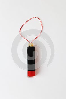 Lipstick as a Christmas tree toy on a red-white string on a white background. Beauty cosmetic New Year concept