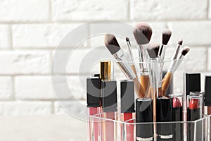 Lipstick holder with different makeup products on table against brick wall, closeup.