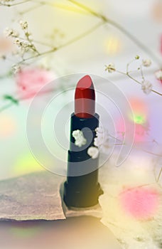 Lipstick on marble podium with flowers, colorful flares and intentional soft light and focus, spring atmospheric mood