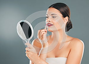 Lipstick, woman and mirror on studio background for beauty, fashion and aesthetics. Young model, red lips and makeup