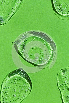 Liquid gel cosmetic smudge on green background. Transparent drops of hyaluronic acid. Beauty and skin care concept