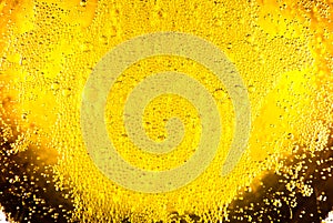 Liquid gold-yellow gasoline bubbles background on beer or champagne glass. Close up, macro shot