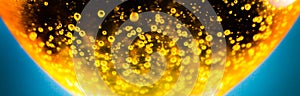 Liquid gold-yellow gasoline bubbles background on beer or champagne glass. Close up, macro shot. Soft focus photo