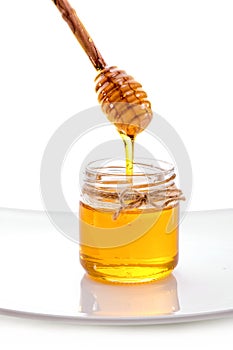Liquid honey flowing off dipper into jar close-up isolated on white background