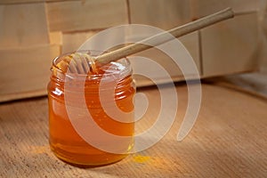 Liquid honey with a honey dipper in a glass jar on a wooden table. Healthy organic honey