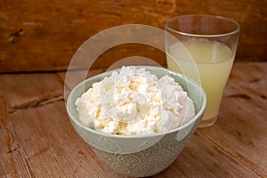 Liquid milk whey in a glass and cottage cheese in bowl on rustic wooden background. Dairy production
