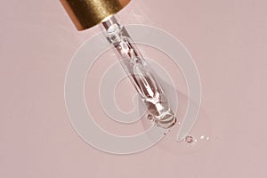 Liquid oil serum drop in pipette isolated on pastel pink background. Retinol, aha, bha acid, collagen skincare fluid