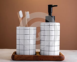 Liquid soap dispenser and  glass with toothbrushes on  wooden tray on  marble table against  brown wall. Composition of toiletries