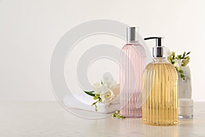 Liquid soap in stylish dispenser, bottle of shower gel, cream, towel and flowers on white table, space for text