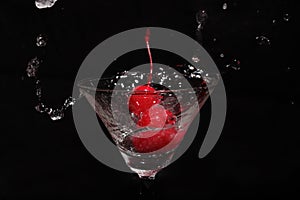 liquid splashing into a glass with cherries in a black background