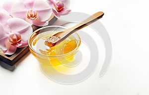 Liquid yellow sugar paste or wax for depilation on a wooden stick on a white background with orchid flowers