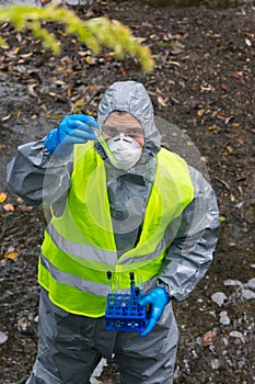 The liquidator of the accident, in a protective suit and a yellow vest, looks at the reaction in a test tube, top view