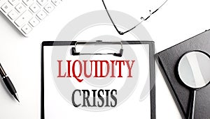 LIQUIDITY CRISIS text written on paper clipboard with office tools