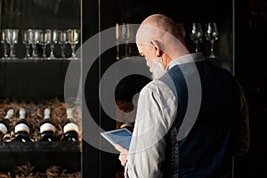 liquor store owner with a digital tablet standing near a rack of wine samples .