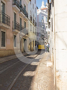 Lisbon, Portugal, October 24, 2021: View of steep narrow Lisbon street with typical yellow vintage tram number 28 line