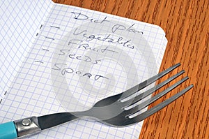 Diet plan concept with a list written in a notebook next to a fork close up