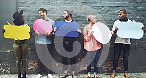 Listen up, theyve got something say. a diverse group of people holding up speech bubbles against a gray brick wall.