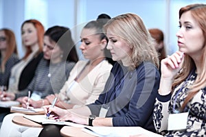 Listeners take notes in notebooks,sitting in the conference room