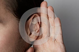 Listening male holds his hand near his ear over grey background.Closeup.