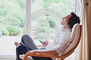 Listening relaxing music at home, relaxed man in headphones sitting in deck chair