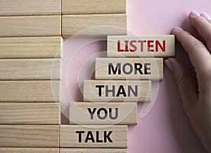 Listening skills symbol. Concept words Listen more than you Talk on wooden blocks. Businessman hand. Beautiful pink background.