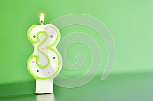A lit candle representing cipher figure three, 3, on green background with copy space.