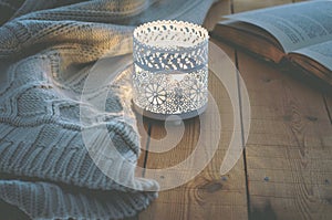 Lit Candle White Knitted Sweater Open Book on Plank Wood Table by Window. Cozy Winter Autumn Evening. Natural Light