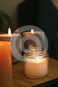 Lit candles in different holders on wooden table indoors