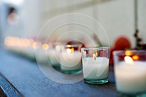 Lit candles and flowers line a shelf on a table outdoors