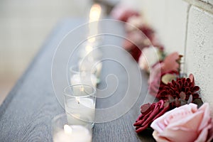 Lit candles and flowers line a shelf on a table outdoors