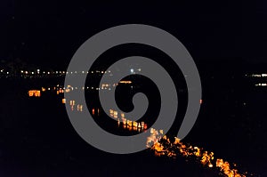 Lit paper lanterns floating on the lake water in a line at dark night