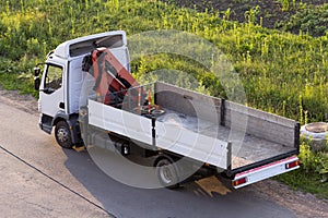 Lit by sun white empty hydraulic truck mounted crane parked on country green grassy roadside. Modern advanced transportation vehic