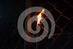 lit torch behind a barbedwire fence in the dark